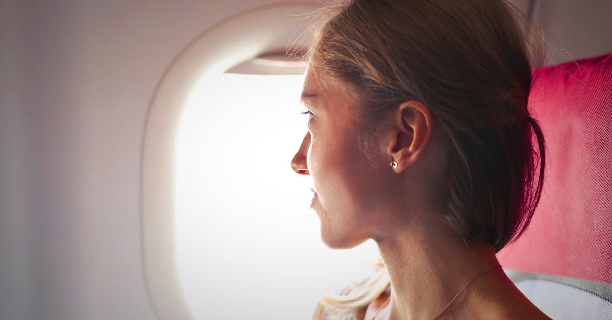 A woman gazes thoughtfully out the window of an airplane during her journey.