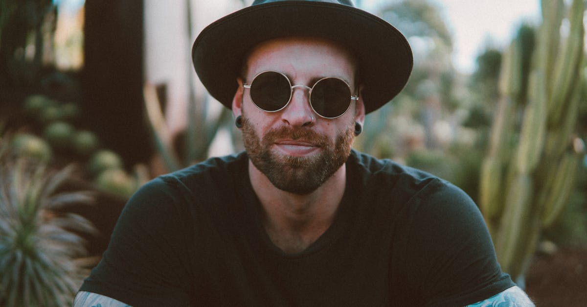 Stylish man with beard and tattoos wearing sunglasses and a hat, enjoying outdoors.