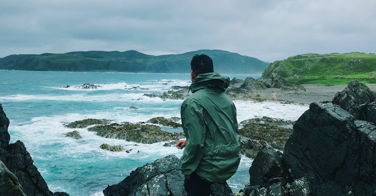 A man in a jacket stands on rocky cliffs overlooking a turbulent sea in Ireland.