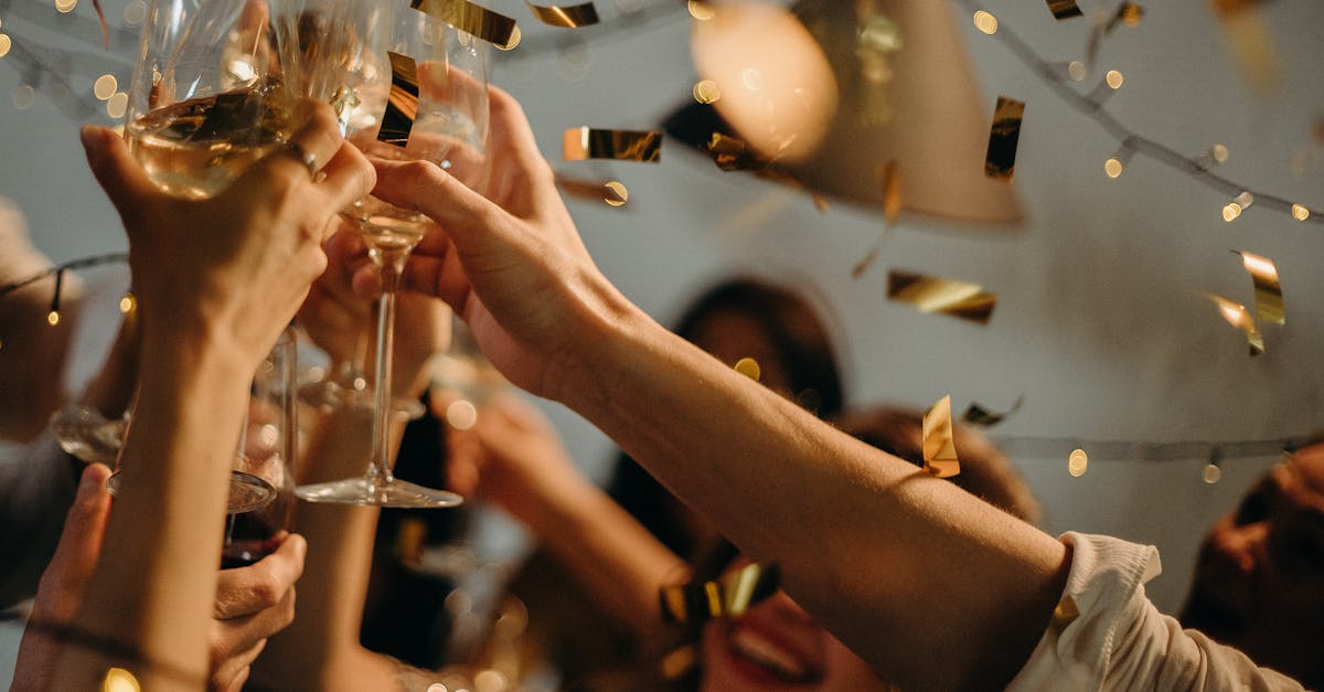 A lively indoor party scene with people toasting champagne glasses amid confetti and warm lights.