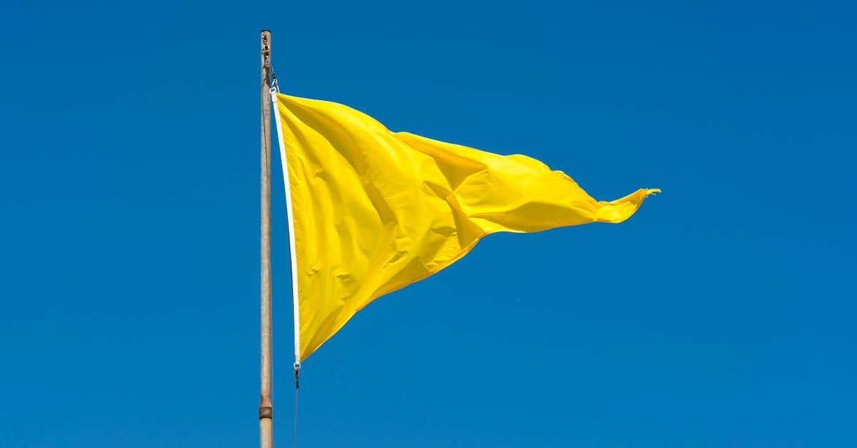 A vibrant yellow flag waving on a pole against a clear blue sky, conveying caution.