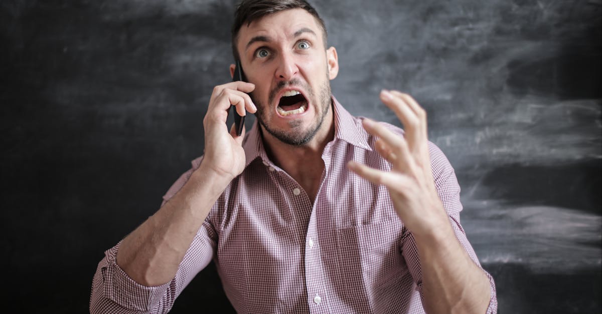 A distressed man in a pink shirt expressing frustration while using a smartphone indoors.