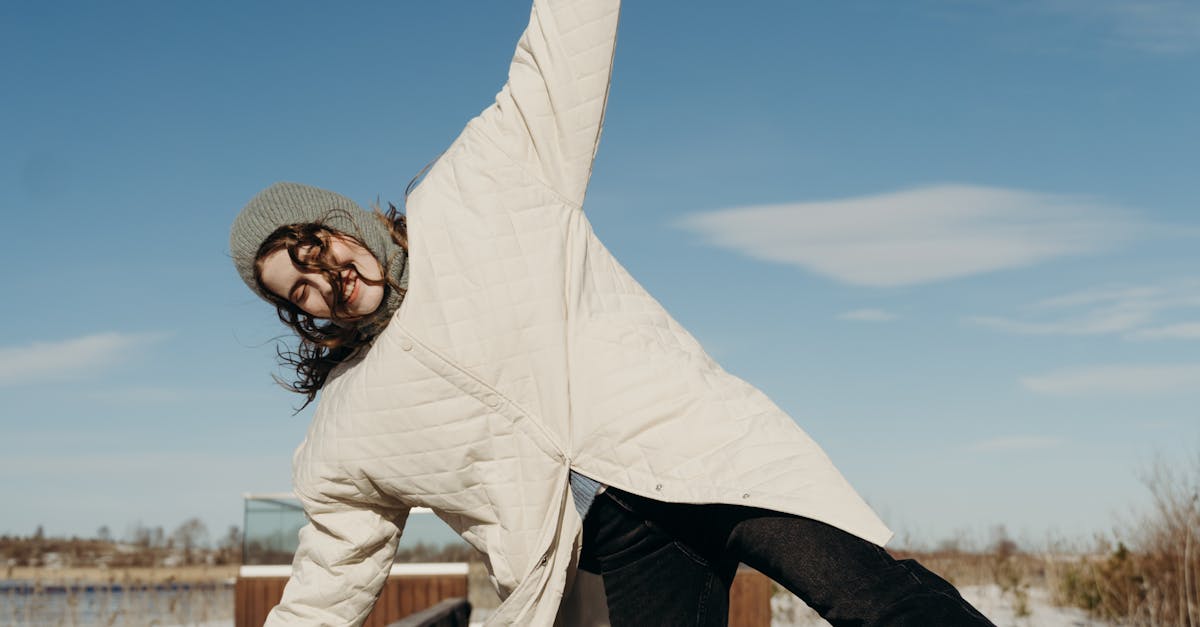 Woman in winter attire playfully posing on a sunlit boardwalk with a clear blue sky.