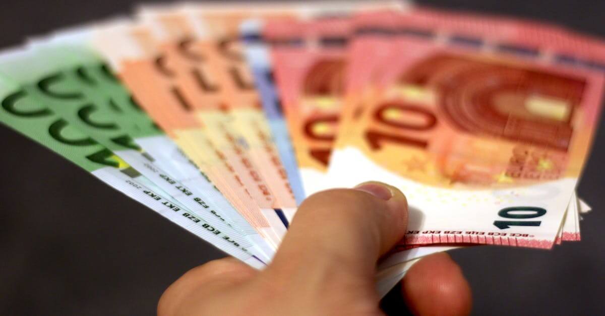 A close-up shot of a hand holding a fan of euro banknotes, symbolizing wealth and currency exchange.